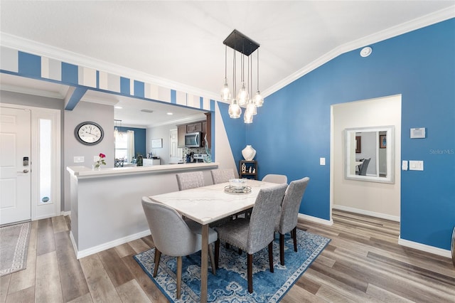 dining area featuring vaulted ceiling, ornamental molding, and wood finished floors