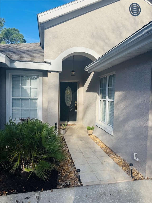 property entrance featuring roof with shingles and stucco siding