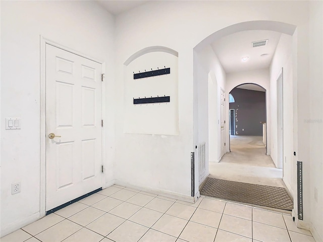 hall featuring arched walkways, visible vents, light carpet, and light tile patterned floors