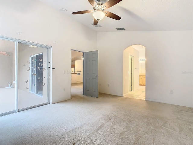 unfurnished bedroom with arched walkways, light colored carpet, visible vents, a ceiling fan, and ensuite bath