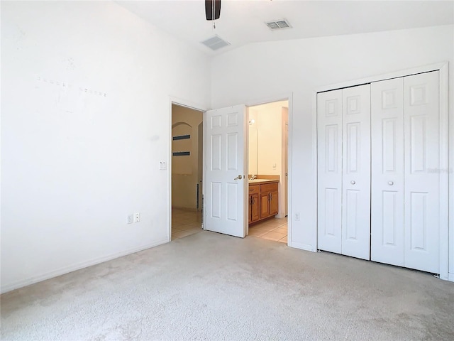 unfurnished bedroom with lofted ceiling, connected bathroom, light carpet, visible vents, and a closet