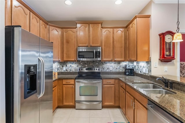 kitchen with tasteful backsplash, hanging light fixtures, appliances with stainless steel finishes, a sink, and dark stone countertops