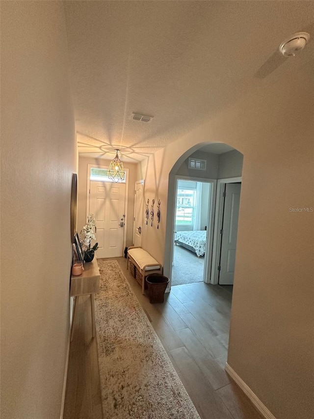 hall with arched walkways, visible vents, baseboards, and wood finished floors