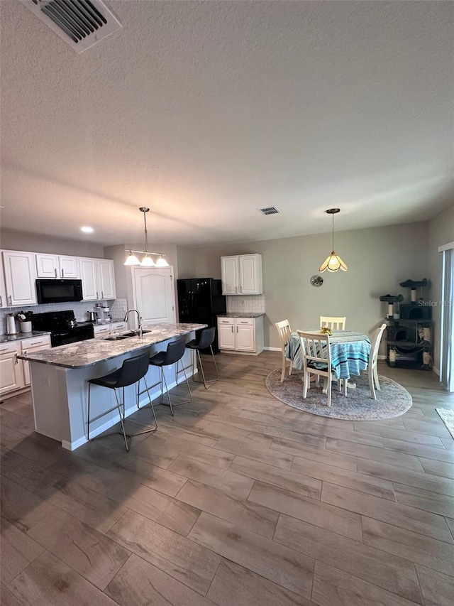 kitchen featuring pendant lighting, a center island with sink, a breakfast bar area, white cabinetry, and black appliances