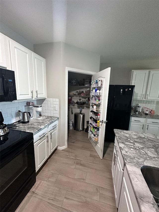 kitchen featuring black appliances, light stone counters, white cabinets, and backsplash