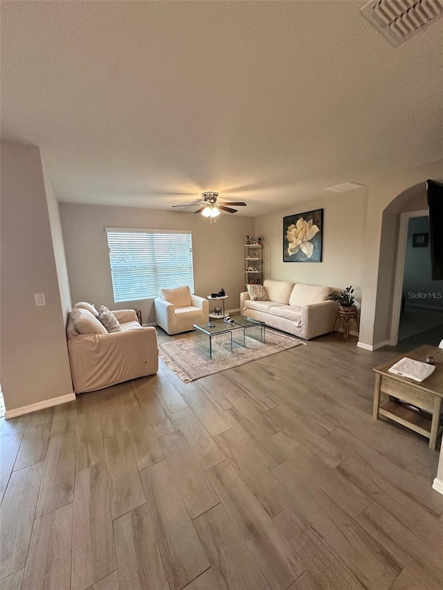 living area featuring ceiling fan, arched walkways, wood finished floors, visible vents, and baseboards