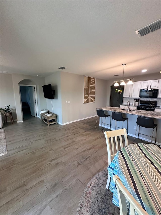 dining area with arched walkways, visible vents, light wood-style flooring, a textured ceiling, and baseboards