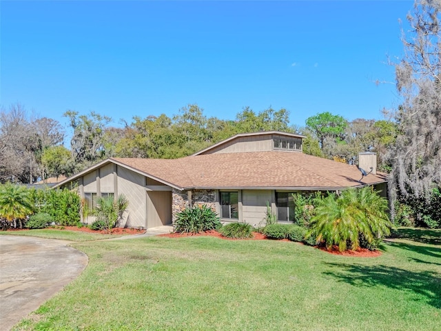 view of front facade with roof with shingles, a chimney, concrete driveway, and a front yard