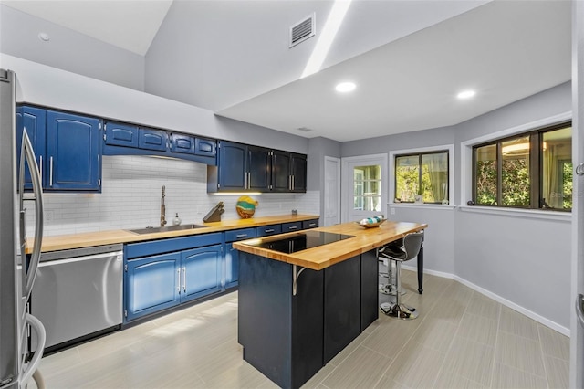 kitchen with butcher block counters, a kitchen bar, stainless steel appliances, blue cabinets, and a sink