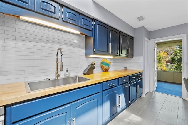 kitchen with butcher block countertops, visible vents, backsplash, and a sink