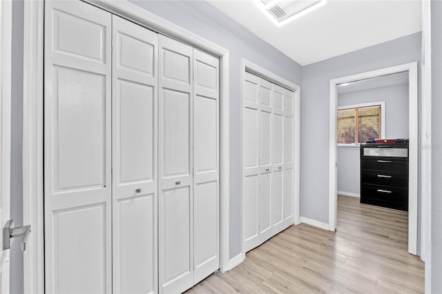 hall featuring visible vents, baseboards, and light wood-type flooring