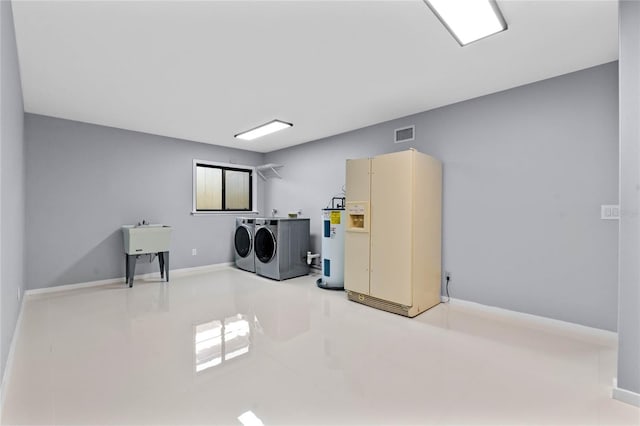 clothes washing area featuring visible vents, electric water heater, baseboards, washing machine and dryer, and a sink