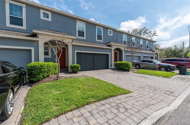 multi unit property with an attached garage, a front yard, decorative driveway, and stucco siding