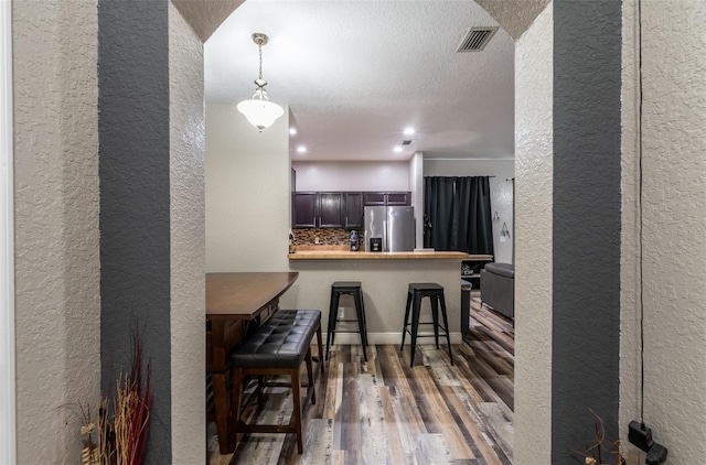 kitchen with stainless steel fridge with ice dispenser, visible vents, a textured wall, a peninsula, and a kitchen breakfast bar