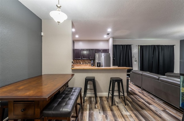 kitchen featuring dark wood-style floors, backsplash, stainless steel fridge, a peninsula, and a kitchen bar