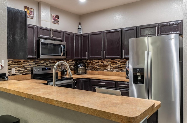 kitchen with appliances with stainless steel finishes, light countertops, a peninsula, and decorative backsplash