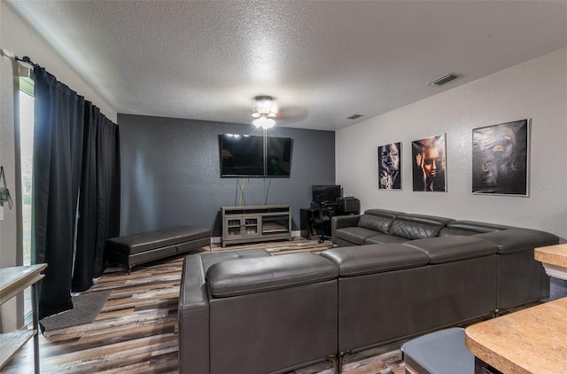 living area with visible vents, a textured wall, a textured ceiling, and wood finished floors