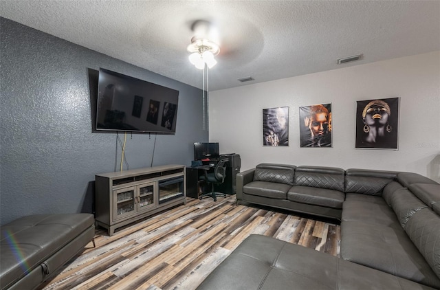 living area featuring a textured ceiling, a textured wall, wood finished floors, and visible vents