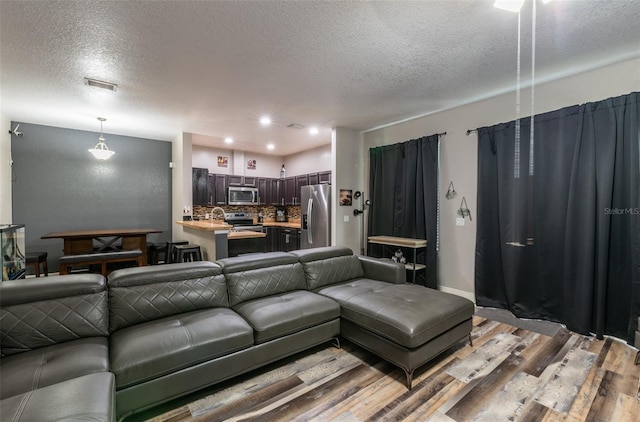 living room with a textured ceiling, recessed lighting, visible vents, baseboards, and light wood-type flooring