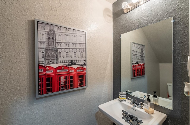 bathroom featuring vaulted ceiling, a textured wall, a sink, and toilet