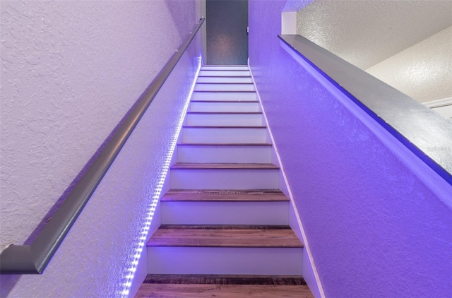 staircase featuring wood finished floors and a textured wall