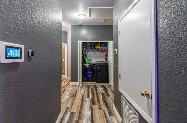 corridor with a textured ceiling, a textured wall, wood finished floors, visible vents, and washer and dryer