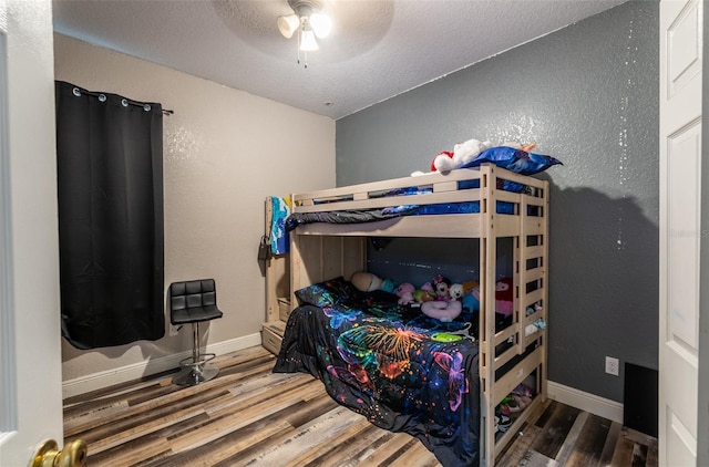 bedroom featuring a textured ceiling, a textured wall, wood finished floors, and baseboards