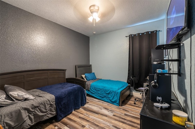 bedroom with a textured ceiling, a textured wall, wood finished floors, and a ceiling fan