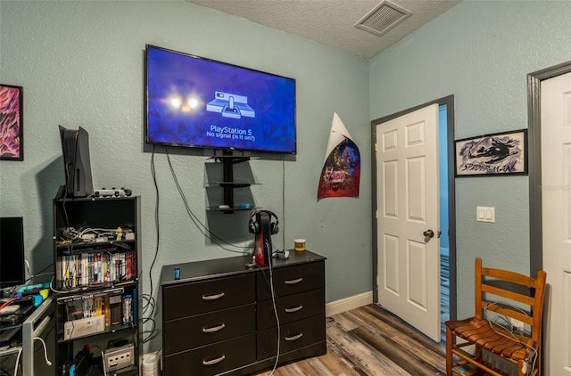 bedroom featuring visible vents, a textured ceiling, baseboards, and wood finished floors