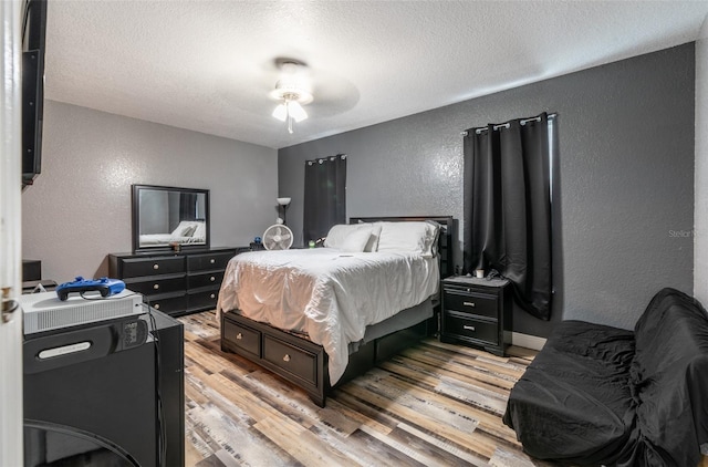 bedroom featuring light wood-type flooring, ceiling fan, a textured ceiling, and a textured wall