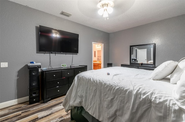 bedroom with baseboards, visible vents, connected bathroom, a textured wall, and wood finished floors