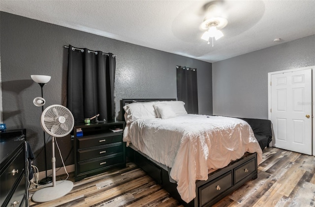 bedroom with a textured wall, ceiling fan, a textured ceiling, wood finished floors, and baseboards