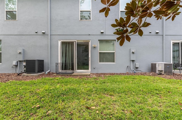 rear view of property featuring stucco siding, a yard, and central air condition unit