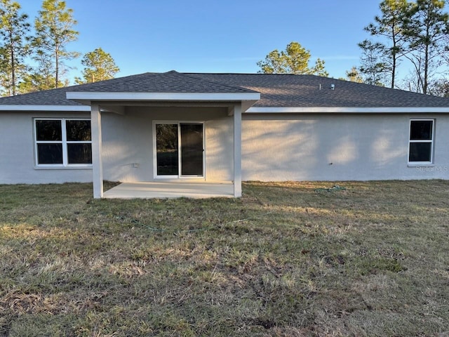 back of property with a patio area, a shingled roof, and a lawn