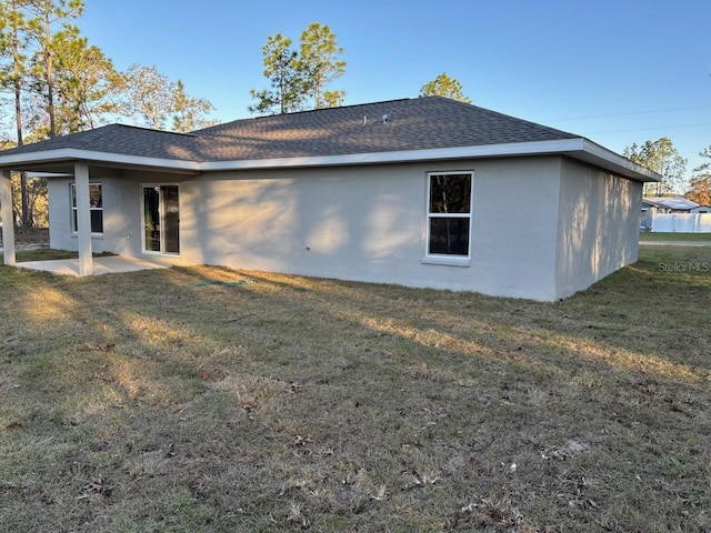 rear view of property featuring stucco siding, a lawn, and roof with shingles