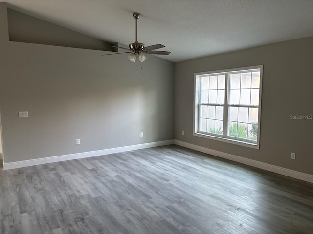 empty room featuring lofted ceiling, ceiling fan, wood finished floors, and baseboards