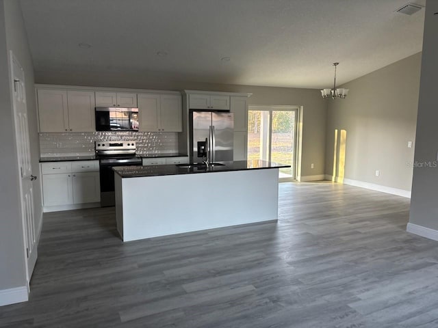 kitchen with stainless steel appliances, dark countertops, visible vents, white cabinetry, and an island with sink