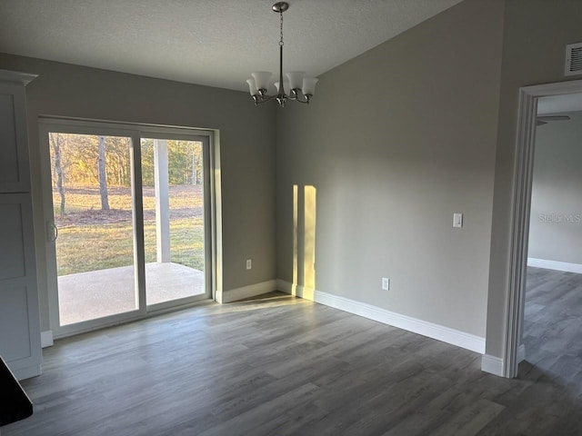 unfurnished dining area with a notable chandelier, a textured ceiling, baseboards, and wood finished floors