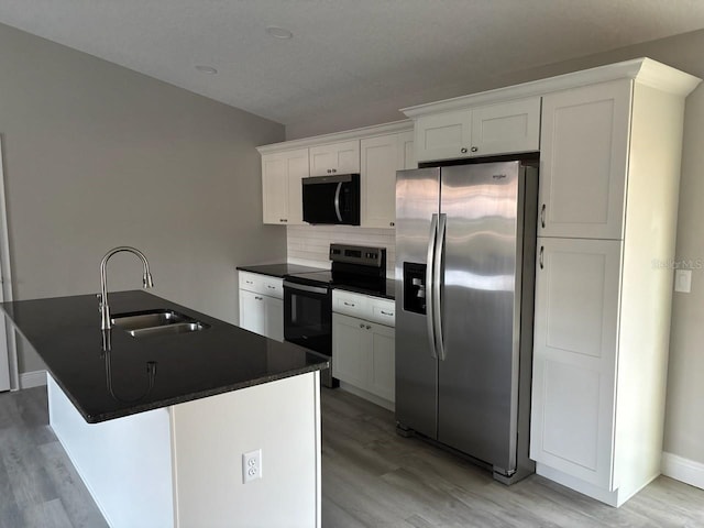 kitchen featuring dark countertops, white cabinets, a sink, stainless steel fridge, and black range with electric cooktop