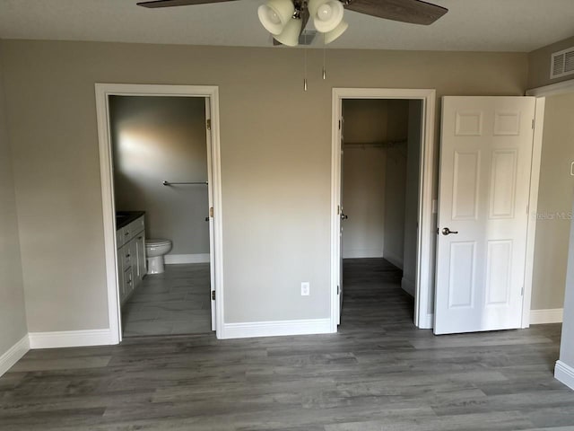 unfurnished bedroom featuring baseboards, a spacious closet, a closet, dark wood-style floors, and ensuite bath