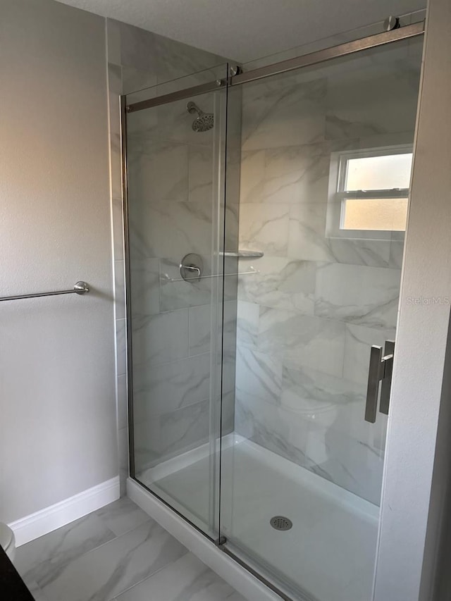 bathroom with marble finish floor, a shower stall, and baseboards