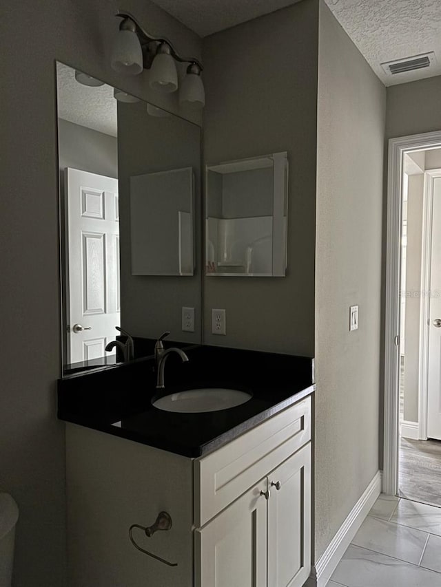 bathroom with marble finish floor, visible vents, a textured ceiling, vanity, and baseboards