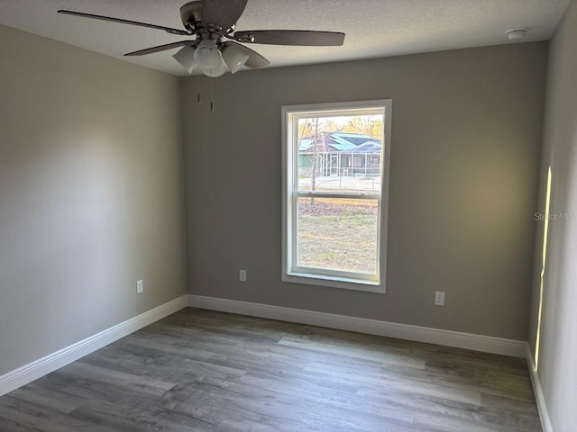 unfurnished room with ceiling fan, a textured ceiling, baseboards, and wood finished floors