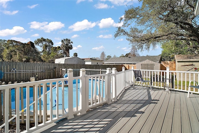 wooden deck with a fenced in pool, a fenced backyard, an outdoor structure, and a shed