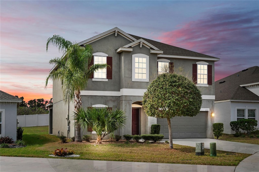 traditional-style house featuring driveway, a garage, fence, a yard, and stucco siding