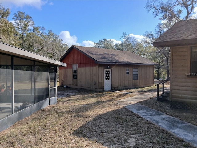 view of property exterior featuring a yard, a shingled roof, and a sunroom