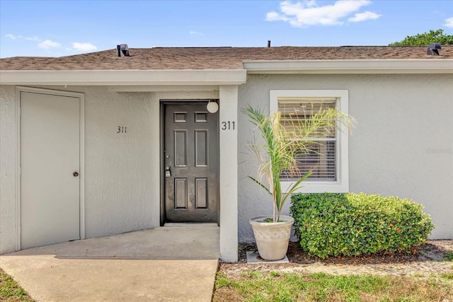 entrance to property with a shingled roof and stucco siding