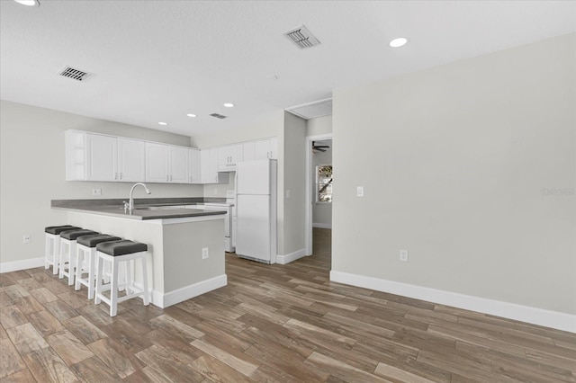 kitchen featuring a peninsula, dark wood-style flooring, white cabinets, freestanding refrigerator, and dark countertops