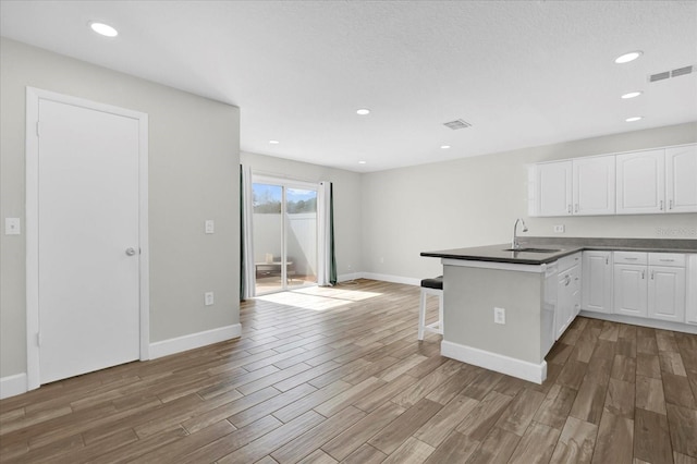 kitchen with dark countertops, light wood-style floors, white cabinetry, a sink, and a peninsula