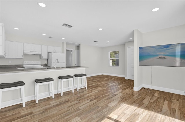 kitchen featuring white appliances, visible vents, white cabinets, under cabinet range hood, and a kitchen bar